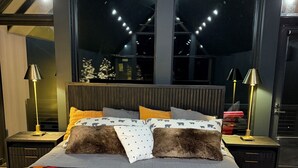 Et soveværelse med en stor seng, to sengeborde og udsigt til natteshimlen gennem store vinduer.