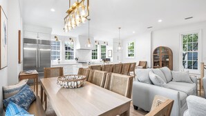 A modern kitchen with stainless steel appliances, a dining area with a wooden table and chairs, and a living area with a sofa and cushions. - Second Wind - Rosemary Beach - Private Pool, Access to Private Beach, Fitness and Tennis Access! (Rosemary Beach)