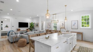 A spacious living room with a large sofa, a dining area, and a kitchen with white cabinetry and a marble island. - Second Wind - Rosemary Beach - Private Pool, Access to Private Beach, Fitness and Tennis Access! (Rosemary Beach)