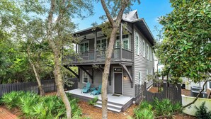 A two-story house with a porch, a balcony, and a fenced yard with tropical plants. - Second Wind - Rosemary Beach - Private Pool, Access to Private Beach, Fitness and Tennis Access! (Rosemary Beach)