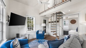 Un vaste salon doté d’un grand téléviseur à écran plat, d’un escalier et d’un coin salon confortable avec des canapés bleus et gris.