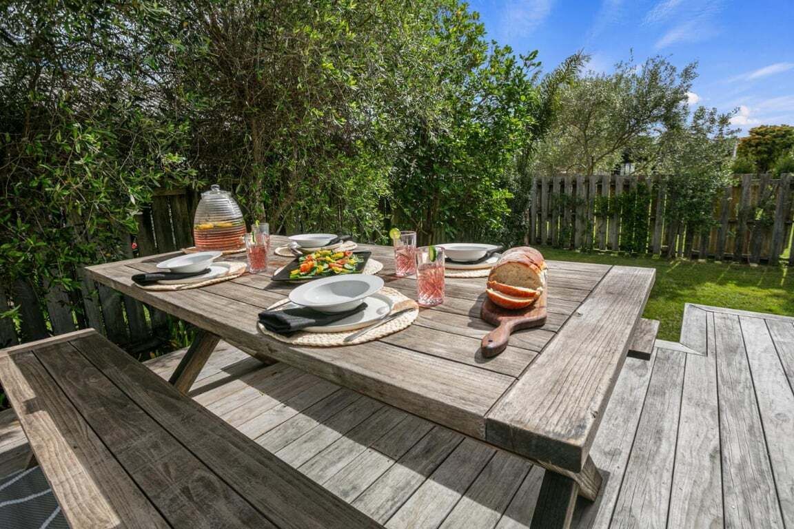 Une table de pique-nique en bois, installée à l’extérieur, avec des assiettes, des verres et un panier de pain.