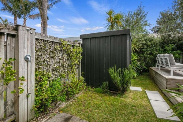 A backyard with a wooden fence, a small shed, and a patio area with a chair. - Relax on Williamson - Whangamata (Whangamata)