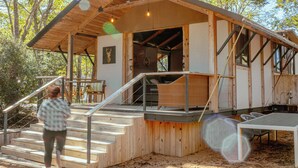 A rustic cabin with a wooden exterior, a staircase leading to a covered porch, and a dining area with outdoor seating. - GLAT Austin (Bastrop)