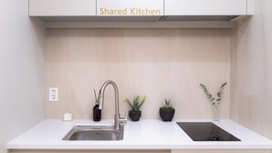 Eine Gemeinschaftsküche mit Spüle aus Edelstahl, einem modernen Wasserhahn und Zimmerpflanzen.