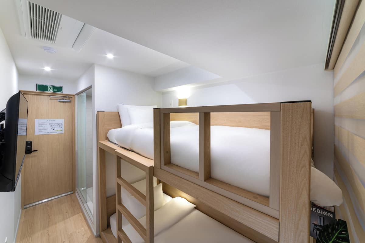 Ein kleines Hotelzimmer mit Etagenbett, Schreibtisch und Toilette.