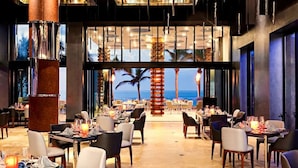A spacious dining area with tables set for guests, large windows offering a view of the ocean, and a modern interior design. - Garza Blanca Resort & Spa Los Cabos (Cabo San Lucas)