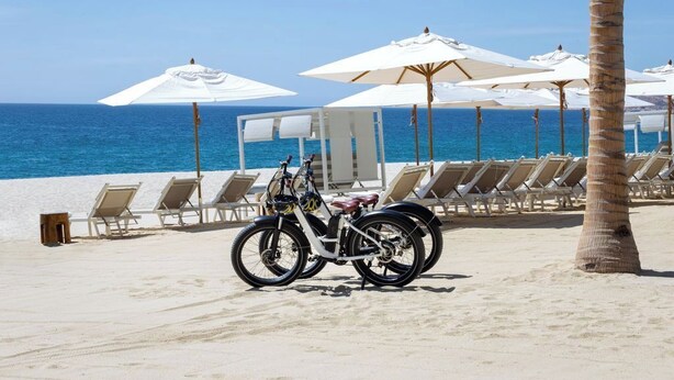 A beach with white umbrellas, lounge chairs, and a bicycle. - Garza Blanca Resort & Spa Los Cabos (Cabo San Lucas)