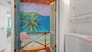 Una stanza con una porta che dà su un balcone affacciato sul mare e sulle palme.