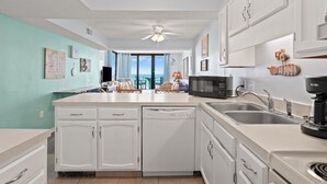 Una cucina con mobili bianchi, un forno a microonde, una macchina da caffè e vista sull'oceano.