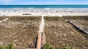 Una spiaggia con una passerella di legno che conduce all'acqua, sabbia fine e cielo sereno.