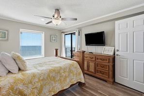 Ein Schlafzimmer mit Bett, Deckenventilator, Kommode, Fernseher und einer Tür.