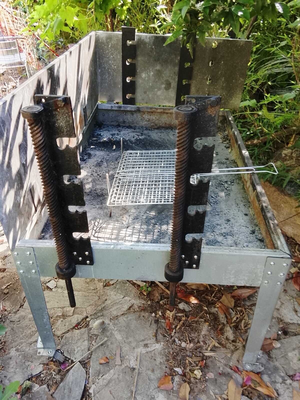Une grille métallique surmontée d’une étagère en fil de fer, le tout entouré de verdure.