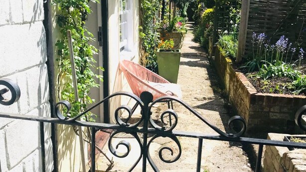 A narrow garden path with a metal gate, potted plants, and a bench. - Mews Cottage off Marlborough High Street (Marlborough)