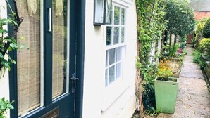 A white building with a black door and windows, surrounded by greenery and a stone pathway. - Mews Cottage off Marlborough High Street (Marlborough)