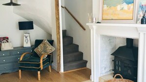 A cozy living room with a dark green armchair, a wooden staircase, a fireplace, and a rustic wooden floor. - Mews Cottage off Marlborough High Street (Marlborough)