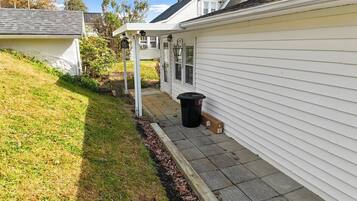 Een huis met een overdekte veranda, een zwarte vuilnisbak en een kleine tuin.