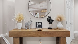 A wooden console table with a round mirror, a 'Relax' sign, decorative items, and a 'Welcome' sign. - Luxury Escape on Mondego Dr – Pool, Spa & Pool Table (Bakersfield)