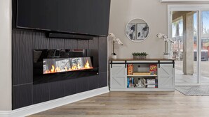 A modern living room with a fireplace, a mounted TV, and a bookshelf with board games. - Luxury Escape on Mondego Dr – Pool, Spa & Pool Table (Bakersfield)