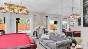 A modern living room with a pool table, a grey sofa, and a billiards table. - Luxury Escape on Mondego Dr – Pool, Spa & Pool Table (Bakersfield)