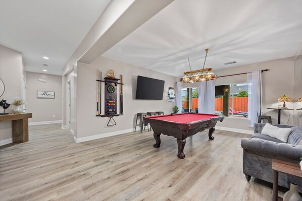 A spacious living room with a pool table, a clock, and a television. - Luxury Escape on Mondego Dr – Pool, Spa & Pool Table (Bakersfield)