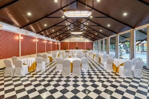 Un salón de banquetes con suelo a cuadros, mesas blancas con cintas doradas y una gran lámpara de araña.