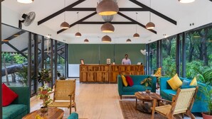 Een ruime lobby met een receptiebalie, groene banken, houten stoelen en grote ramen met uitzicht op het omliggende landschap.