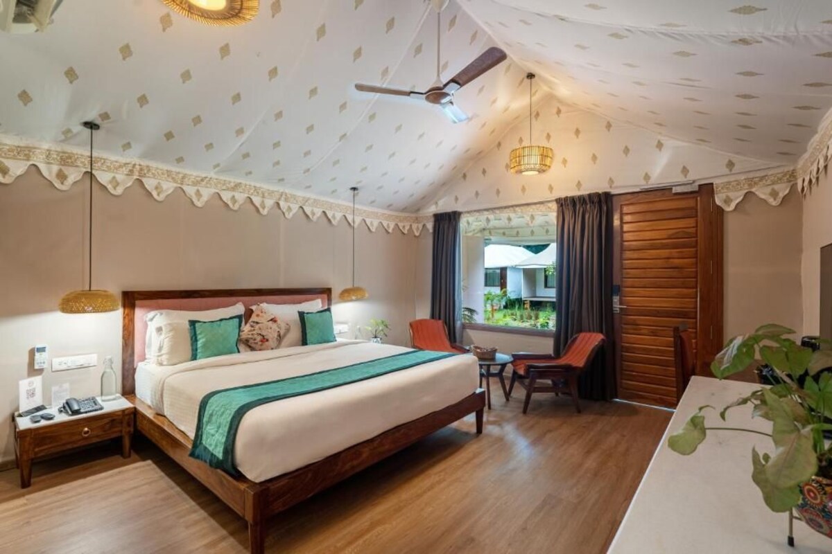 Een hotelkamer met een groot bed, een bureau, een stoel, een plafondventilator en een raam met gordijnen.