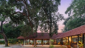 A courtyard with a covered seating area and a building with a tiled roof. - Aranya Vilas - A Nature Resort (Udaipur)