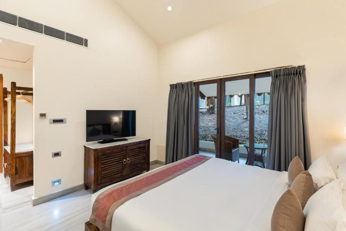 Un dormitorio con una cama grande, un televisor sobre un aparador de madera y vista a un patio a través de una puerta corrediza.