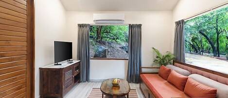 A living room with a TV, wooden furniture, a sofa, and a view of greenery.