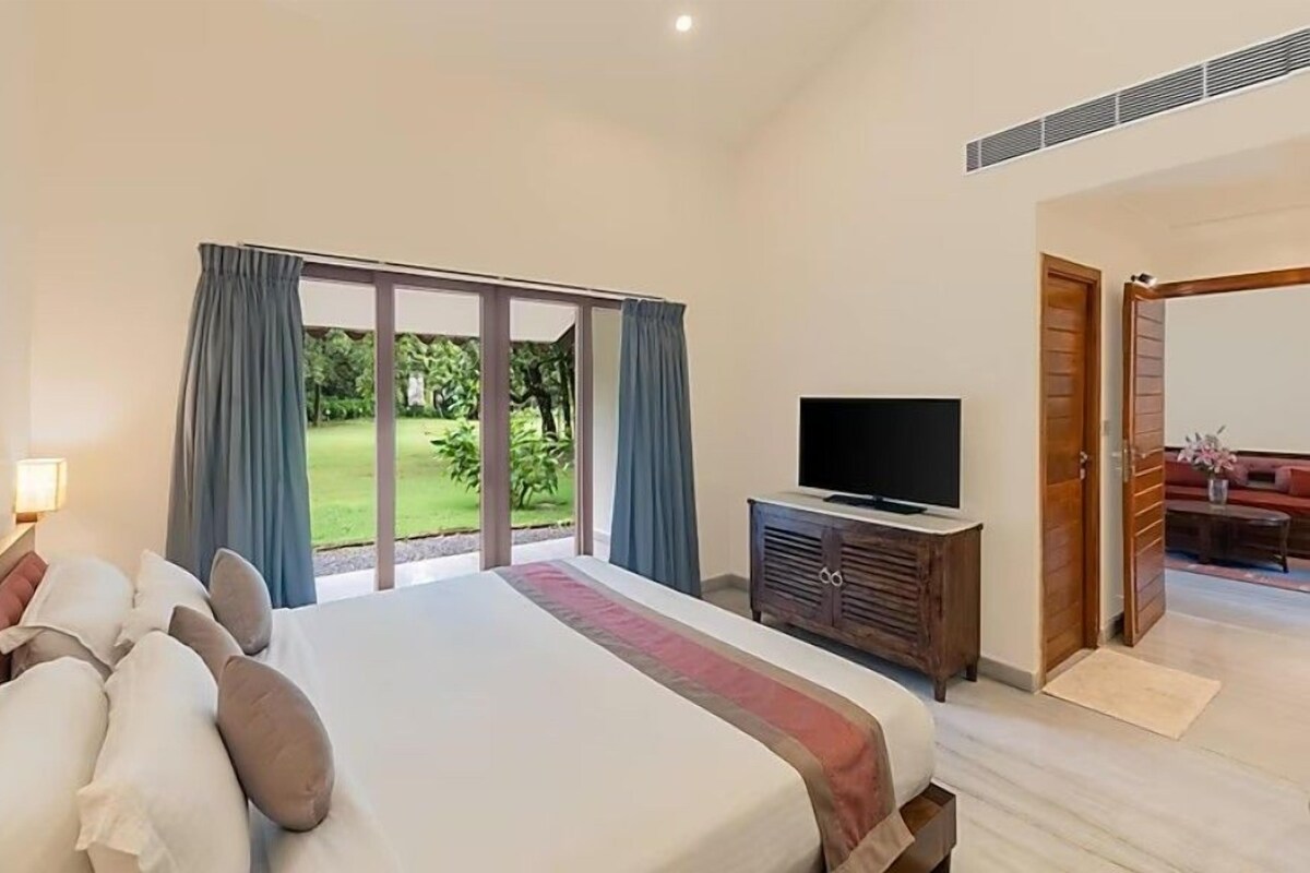 Un dormitorio con una cama grande, un televisor sobre un mueble de madera y una puerta corrediza de vidrio que da a un jardín.