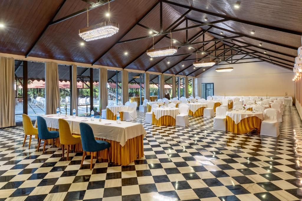 Un amplio salón con suelo a cuadros, mesas dispuestas para comer y un alto techo con candelabros.