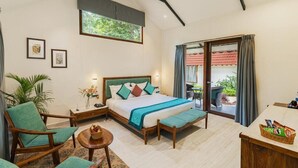 A bedroom with a bed, two chairs, a small table, a nightstand, and a window with curtains. - Aranya Vilas - A Nature Resort (Udaipur)