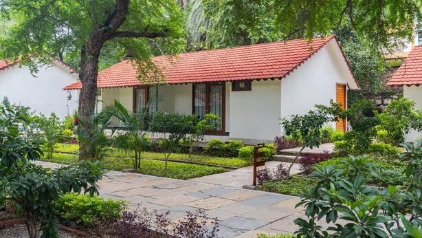 Een bungalow met een rood pannendak, omringd door weelderige begroeiing en een stenen pad.