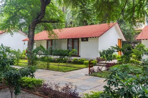 A bungalow with a red-tiled roof, surrounded by lush greenery and a stone pathway. - Aranya Vilas - A Nature Resort (Udaipur)