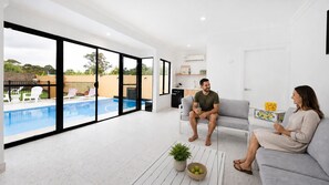 Un saló modern amb vista a la piscina, un sofà, una taula de centre amb una planta i una taula de menjador amb un plat de fruita.