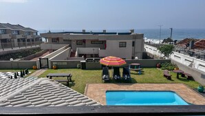 Ein Poolbereich auf dem Dach mit Blick auf das Meer, ein kleiner Garten und ein bunter Sonnenschirm.