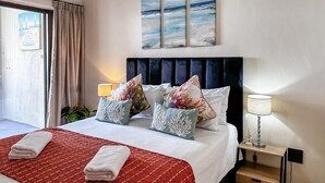 Una camera d'albergo con un letto, due cuscini, una coperta rossa, un comodino con una lampada e un quadro sopra il letto.