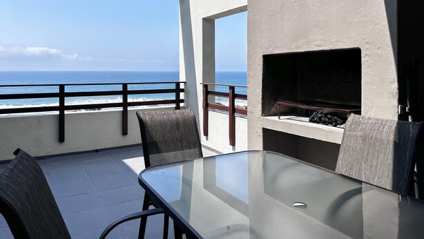 Un balcone con un tavolo e sedie in vetro, vista sull'oceano.