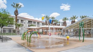 A water play area with colorful arches and a pool, surrounded by palm trees and a building with a covered patio. - Desert Views Retreat, 8 Bedrooms, Sleeps 24, Community Amenities (St. George)
