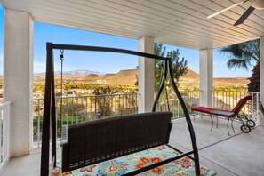 Un espace extérieur abrité comprenant un fauteuil suspendu, un banc rouge et une vue sur un paysage désertique avec des montagnes.