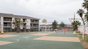 An outdoor basketball court with a net, surrounded by a fence, and adjacent to a multi-story building with balconies. - Desert Views Retreat, 8 Bedrooms, Sleeps 24, Community Amenities (St. George)
