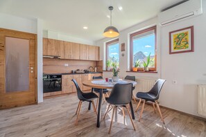 A modern kitchen with wooden cabinets, a dining table with chairs, and a window with plants. - Weiss Family Apartment Savinja Hills, Rečica ob Savinji, Slovenia (Rečica ob Savinji)