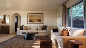 A modern living room with a sofa, a coffee table, and a large window with a view of trees. - Central Park Mid-Century Modern Dream (Midland)