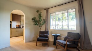 A modern living room with two armchairs, a small round table, a potted plant, and a view of the kitchen through an archway. - Central Park Mid-Century Modern Dream (Midland)