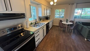 Une cuisine moderne avec des meubles blancs, une cuisinière noire et un coin repas comprenant un canapé vert et une petite table.