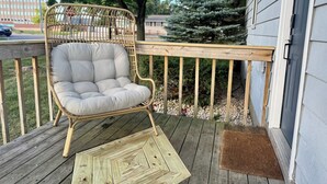 Une chaise en osier sur une terrasse en bois, avec un paillasson marron et une table en bois.