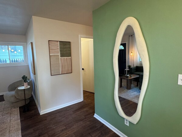 A hallway with a green wall, a large mirror, and a door leading to a living area.