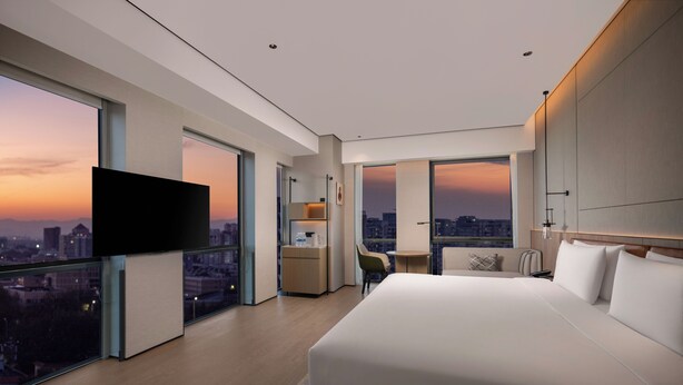 A modern hotel room with a large bed, a desk, a chair, a TV, and a city view. - Holiday Inn Beijing Daxing Centre By Ihg (Daxing)